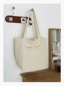 Detail view of large cream canvas tote bag with front pocket hanging on wooden hook