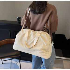 Rear view of a model carrying a beige nylon travel tote with brand embroidery and mesh pocket