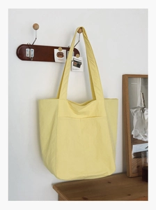Close-up of yellow canvas tote bag with functional front pockets hanging on wall