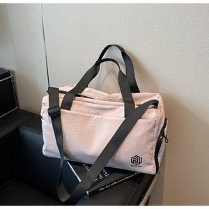 Detail of light pink large travel bag with durable black straps and logo on a leather bench