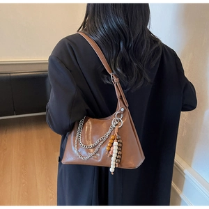 Close-up of brown leather shoulder bag with silver chains and ethnic tassel pendant detail
