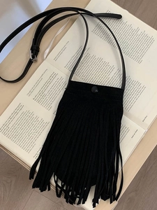 Petit sac bandoulière noir à franges en daim posé sur un livre de style vintage