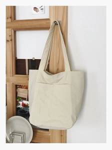 Detail of minimalist cream canvas tote bag with front pocket hanging on wooden frame