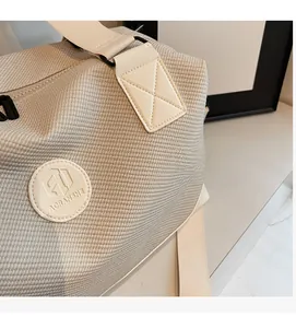 Detail of light beige knitted travel bag featuring textured fabric and leather logo patch