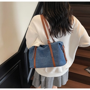 Dettaglio della borsa da viaggio in denim blu con finiture in pelle marrone e fibbia