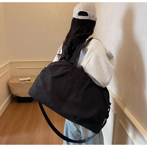 Detail of a large black nylon travel bag with shoulder strap worn by a model