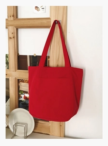 Detail of red canvas tote bag with large front pocket hanging on a wooden window