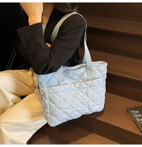 Close-up of quilted light blue nylon tote bag showing diamond stitching and brand label