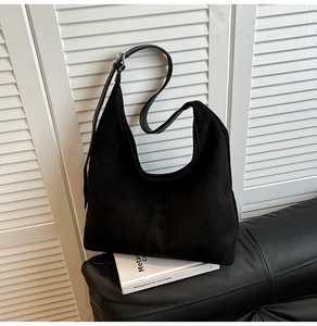 Detailed view of large black suede shoulder bag with vertical stitching on white books