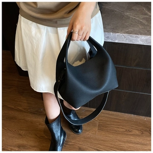 Close-up of black lychee grain leather bucket bag with top handle and wide shoulder strap