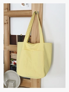 Detail of minimalist pale yellow tote bag with front dual pockets hanging on a door hook