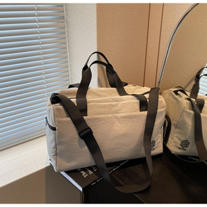 Close-up of cream travel bag with NING JIA logo, black straps on a black desk with books