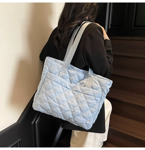 Close-up of quilted pattern and woven label on a light blue nylon tote shoulder bag