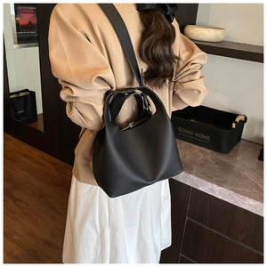 Detail view of black lychee grain leather bucket bag with wide shoulder strap on model