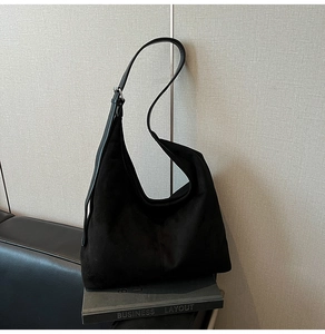Detail of black suede hobo bag with adjustable leather strap on a decorative book