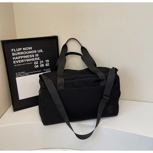 Detail of minimalist black travel bag featuring durable handles and adjustable shoulder strap