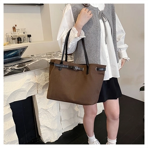 Detail of dark brown canvas tote bag featuring decorative leather strap and black handles