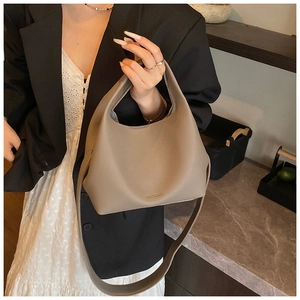 Detail of taupe pebbled leather bucket bag styled with a black blazer and white skirt