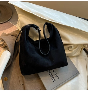 Detail of black suede hobo shoulder bag placed on a brown blazer and grey books