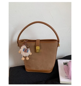 Detail of a brown suede bucket bag featuring a gold twist lock and cute plush lamb charm