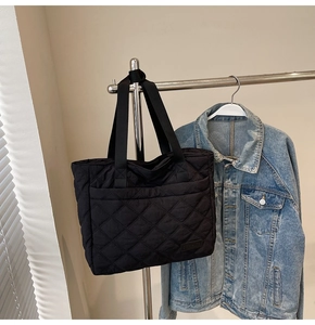Detail of black quilted tote bag with large outer pocket hanging on a metal rack
