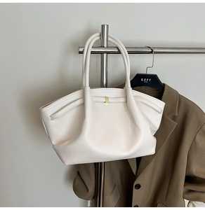 Close-up of pleated cream leather tote bag with gold buckle on a stylish suit hanger
