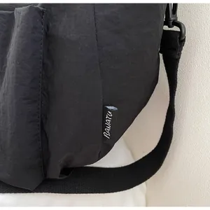 Detail of black nylon shoulder bag showing side pocket, woven strap, and BAIATU label
