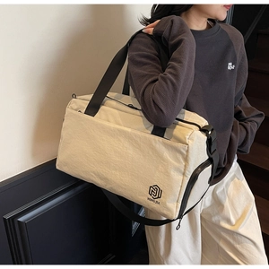 Detail view of large cream travel bag with NING JIA logo and wide black shoulder straps