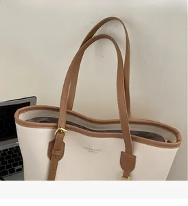 Close-up of contrast large tote bag with brown straps, metal buckles, and top zipper