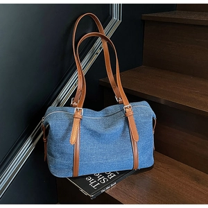 Dettaglio della borsa da viaggio in denim blu con manici in pelle marrone su scale