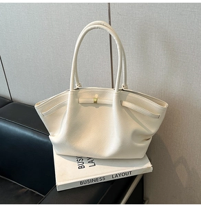 Close-up of cream lychee leather tote bag with decorative drawstring on a book