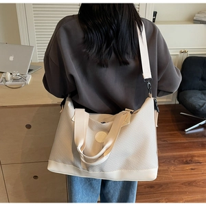Detail of off-white travel tote showing textured fabric and adjustable shoulder strap