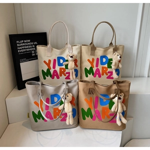 Detailed row of large canvas tote bags in four colors with bear charms and bold text