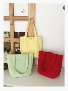 Three canvas tote bags in yellow, green, and red showing durable fabric and front pocket