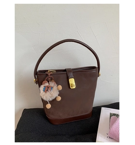 Detail der dunkelbraunen Leder-Eimertasche mit Goldschließe und Plüsch-Anhänger