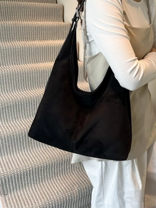 Minimalist black suede tote bag with adjustable leather strap worn as a shoulder bag