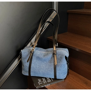 Dettaglio della borsa tote in denim blu con tracolla in pelle marrone e fibbia in argento