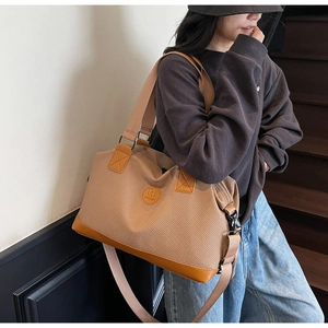 Detail of a large brown travel tote bag with leather logo and adjustable shoulder strap