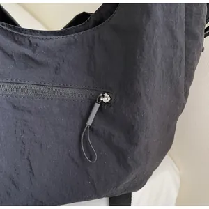 Detail of smooth black nylon crossbody bag featuring a durable zipper with a cord pull