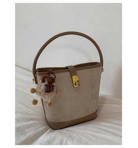 Close-up of beige suede bucket bag with brown leather trim and cute plush bear charm