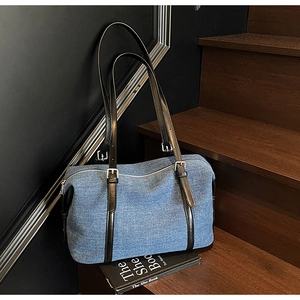 Dettaglio della borsa tote in denim blu con manici in pelle nera su scale di legno