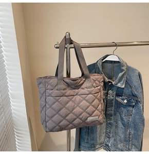 Close-up of diamond quilted taupe tote bag with dual handles and brand logo detail