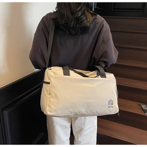 Close-up of a large beige travel tote bag with black straps and brand logo detail