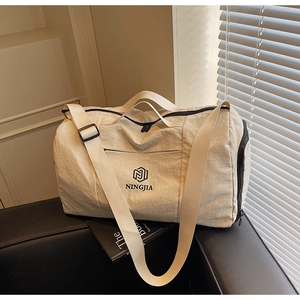 Close-up of cream travel bag with NINGJIA logo and adjustable strap on a leather sofa