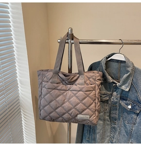 Detail view of khaki quilted tote bag featuring reinforced woven handles and logo pocket