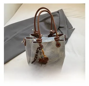 Detail of washed denim bucket bag with brown leather handles and decorative pendant