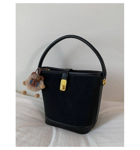 Detail of black bucket bag with matte suede texture and a cute brown bear charm