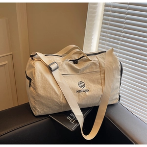 Close-up of beige nylon travel bag with brand logo and adjustable fabric shoulder strap