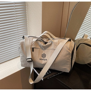 Close-up of light gray travel bag with dual handles and logo detail on black books