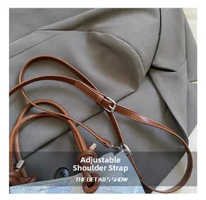 Detail of adjustable leather strap with silver buckle on blue denim bucket bag